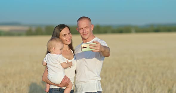 Young Family Takes a Selfie on a Smartphone in a Wheat Field a Photo Shoot