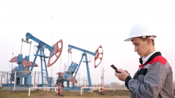 Oil Industry Worker with Phone on the Background of the Oil Pump