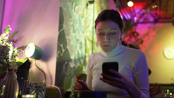 Young Woman Scrolls Through Social Media Eating at Cafe