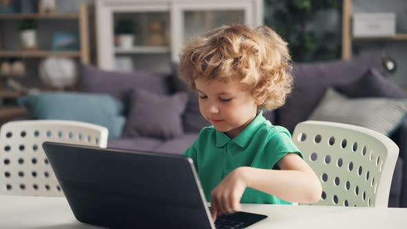 Cute Little Boy Playing with Modern Laptop Pushing Buttons and Smiling at Home