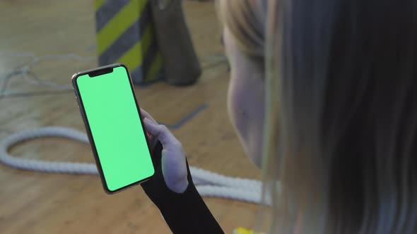 A Young Athletic Woman Holds A Smartphone in Her Hand, Shows A Green Chromakey Screen, Is in The Gym