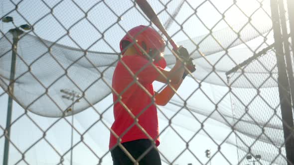 A boy practices little league baseball at the batting cages and bunting the ball.
