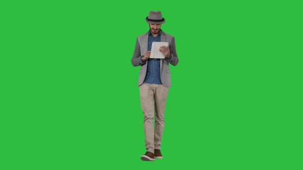 Handsome smiling arab man in a hat walking and using tablet