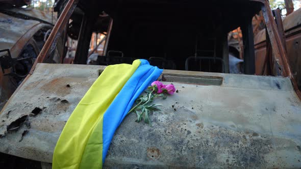 Ukrainian Flag and Purple Flowers on Car Hood of Burnt Out Destroyed Automobile