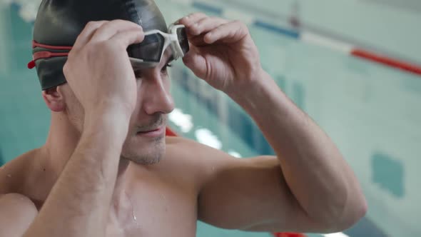 Young Professional Man Swimmer Puts on Glasses for Swimming Training Day in the Pool