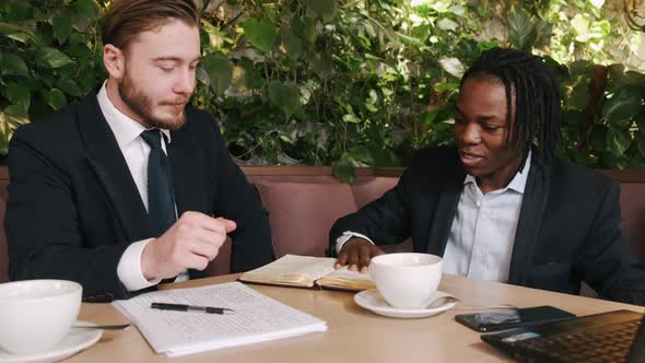 Focused Businessman Talking with Partner and Resding Papers at Restaurant