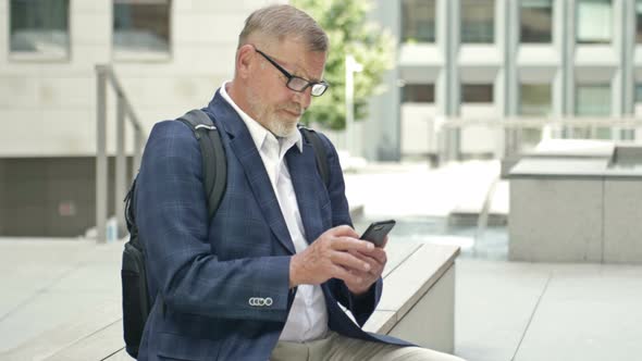 Businessman is a Grayhaired Man in a Business Suit Sitting Near the Office Communicates By Phone