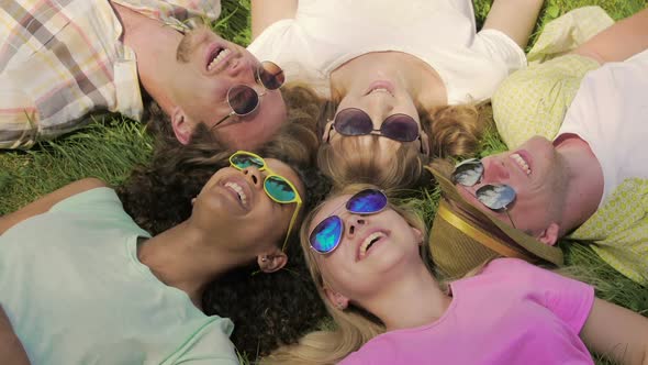 Mixed Race Girl Lying on Grass With Friends, Checking Text on Phone, Laughing