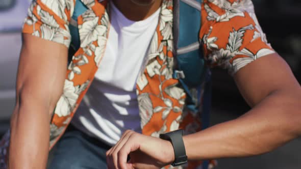 African american man in city, sitting on bike and checking smartwatch in the street