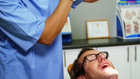 Smiling dentist assistant adjusting dental light over patients mouth