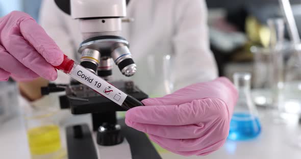 Doctor Holding Test Tube with Positive Blood Test for Covid19 in Front of Microscope in Laboratory