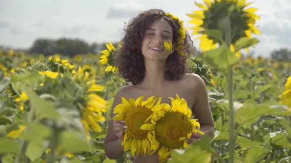 Portrait of Pretty Curly Playful Girl Looking at the Camera Smiling Standing in the Sunflower Field