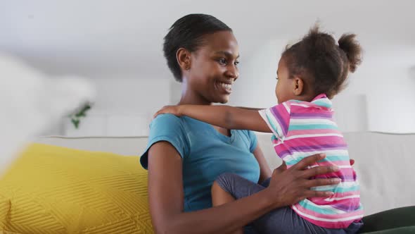 Happy african american mother and daughter sitting on sofa and touching foreheads