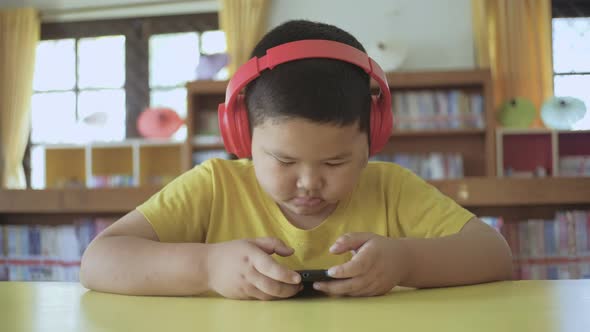 Asian little boy with red headphones using smartphone at home