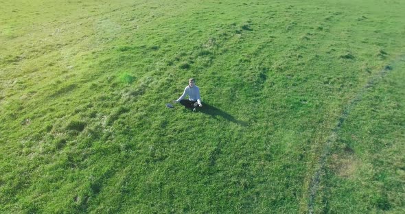 Low Orbital Flight Around Man on Green Grass with Notebook Pad at Yellow Rural Field.