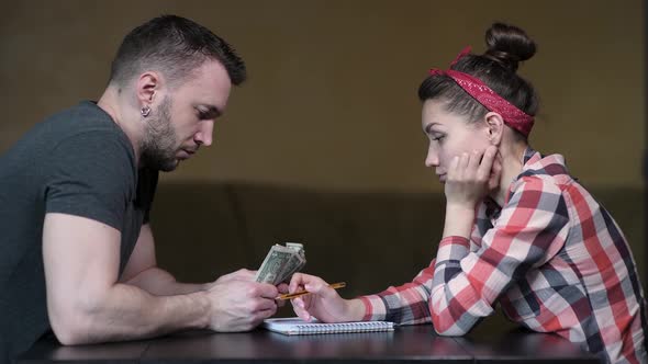 A man and a woman are sitting at the table and counting the rest of the money