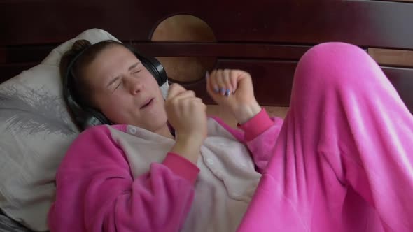 Girl in Pajamas on the Bed Listens to Music Through Headphones and Dances Slowmo