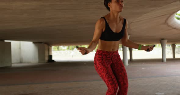 Front view of young African American woman exercising with skipping rope in the city 4k