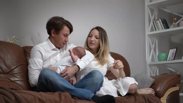 Wide Shot Portrait of Happy Couple of Parents Sitting with Newborn Baby Son on Comfortable Couch in