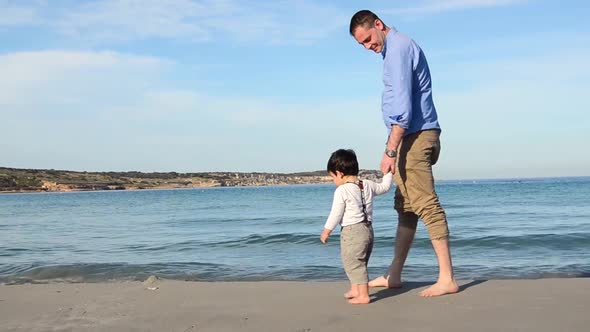 FULL SHOT of father and son walking barefoot along the beach of Malta on a clear beautiful day