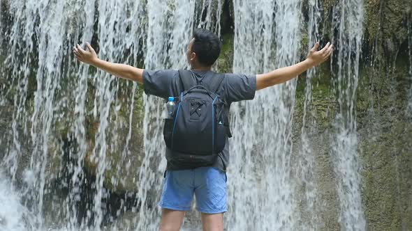 Man Standing With Arms Outstretched In Front Of  Waterfall