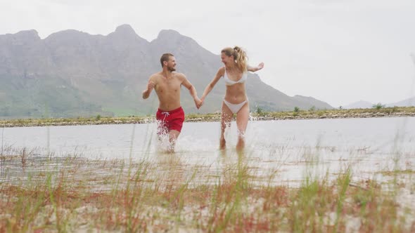 Caucasian couple having a good time on a trip to the mountains, wearing bathing suits, running and j