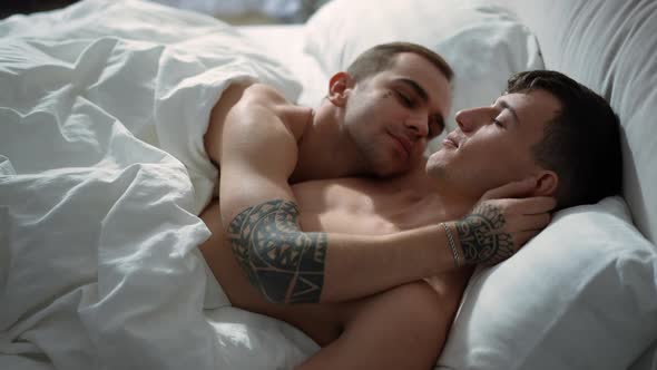 Side View Young Men Sleeping in Bed Together Waking Up in the Morning Kissing Cheek