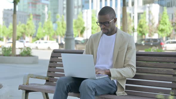 Thinking African Man Using Laptop While Sitting Outdoor on Bench