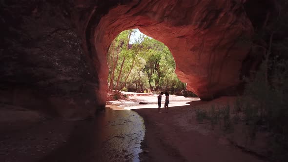 A man getting down on one knee and proposing to his girlfriend under a beautiful huge red rock Arch