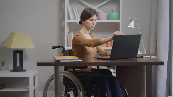 Young Intelligent Concentrated Disabled Woman Sitting at Table Opening Laptop Typing on Keyboard