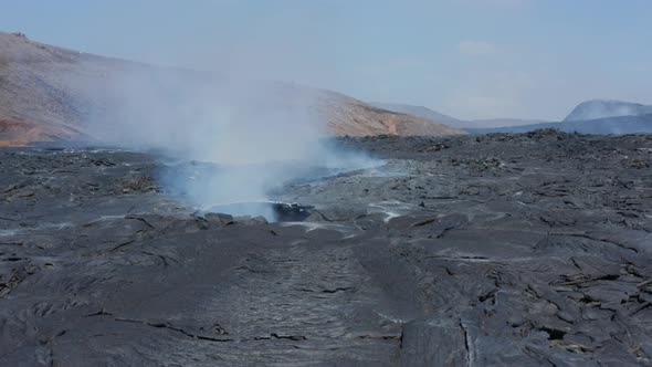 Slide and Pan Footage of Smoke Coming Out From Hole in Layer of Cooling Lava in New Lava Field