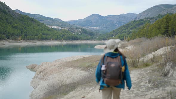 Young Woman in Trekking Gear Walks Away From Camera By Lake in Spain