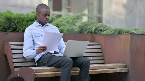 African Man Working on Papers and Laptop Outdoor