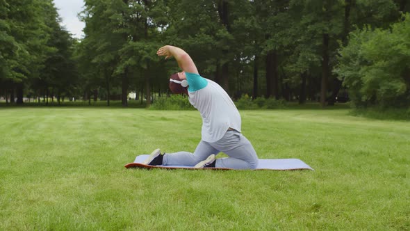 Overweight Young Man Training in Park in Headphones on Sunny Day