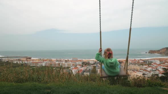 Little Girl Looking at Ocean and Resort Town From the Swing