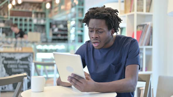 African Man Reacting To Loss on Tablet in Cafe
