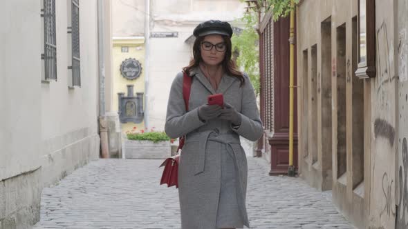 Young Beautiful Girl In Glasses With A Smartphone Walks Down The Street Of The Old City