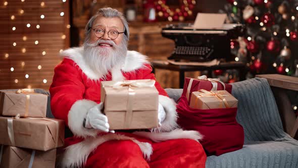 Friendly Man in Santa Claus Costume Giving Wrapped Gift Box