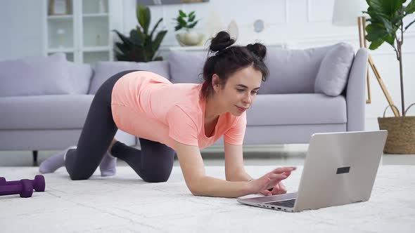 Satisfied Young Woman in Modern Hairstyle Watching Fitness Workout on Laptop