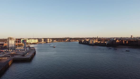 Aerial view of River Thames with cruising boat during sunset and construction site on shore. London,