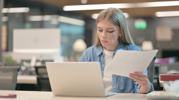 Successful Young Woman Reading Documents While Using Laptop