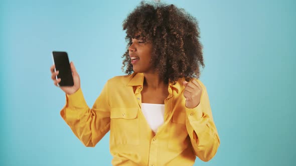 Afro American Lady Looking at Smartphone Saying Yes Showing you the Screen and Smiling Posing on