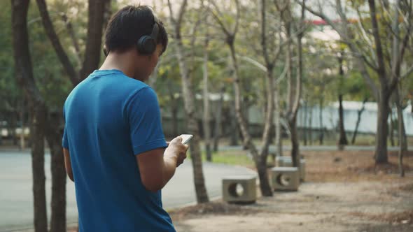 Asian men resting after training outdoors using smartphones while walking in the park environment.