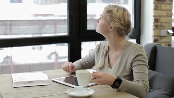 A business girl in a restaurant works with a tablet and drinks coffee.