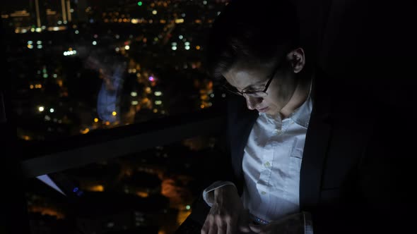 Young Man Freelancer Is Working on His Computer Near the Window in Home at Night