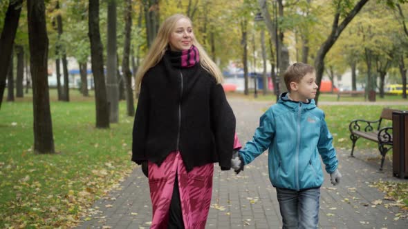 Portrait of Caucasian Woman and Boy Walking in Autumn Park Holding Hands Talking and Leaving