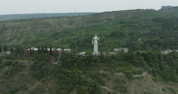 Slow aerial arc shot of the Mother of Georgia statue and Tbilisi landscape.