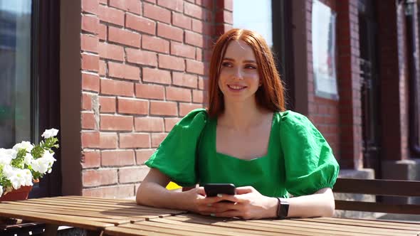 Medium Shot Portrait of Happy Thinking Young Woman Using Typing Mobile Phone Sitting at Table in