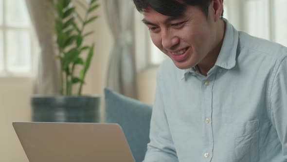 Asian Male Working On Laptop And Smiling At Living Room