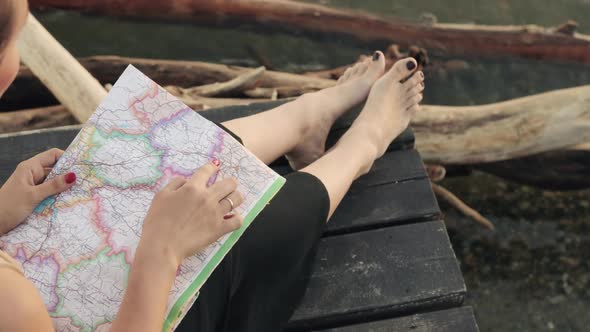 Woman Is Pointing a Route To Destination Sitting on the River Pier, Map Closeup